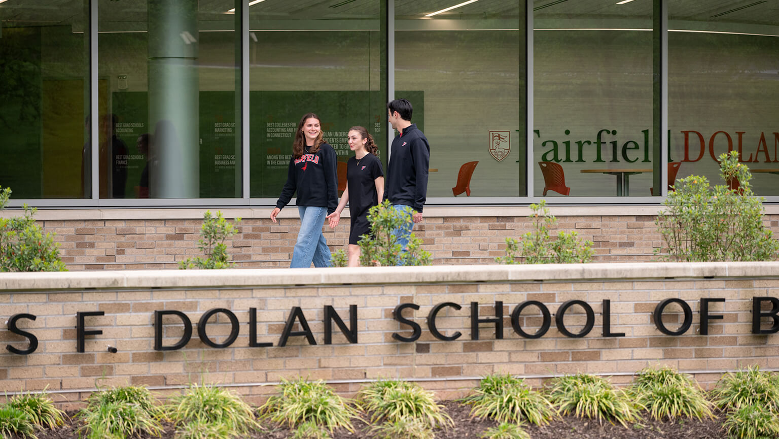 Three individuals stand outside the Charles F. Dolan School of Business, smiling and engaged in conversation.