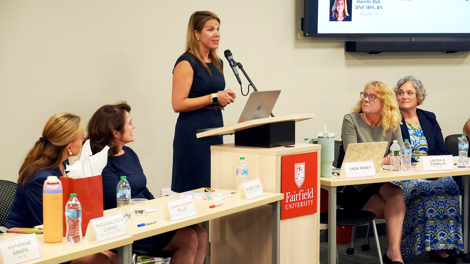 A woman presents to an audience, engaging them with her speech and visual aids.