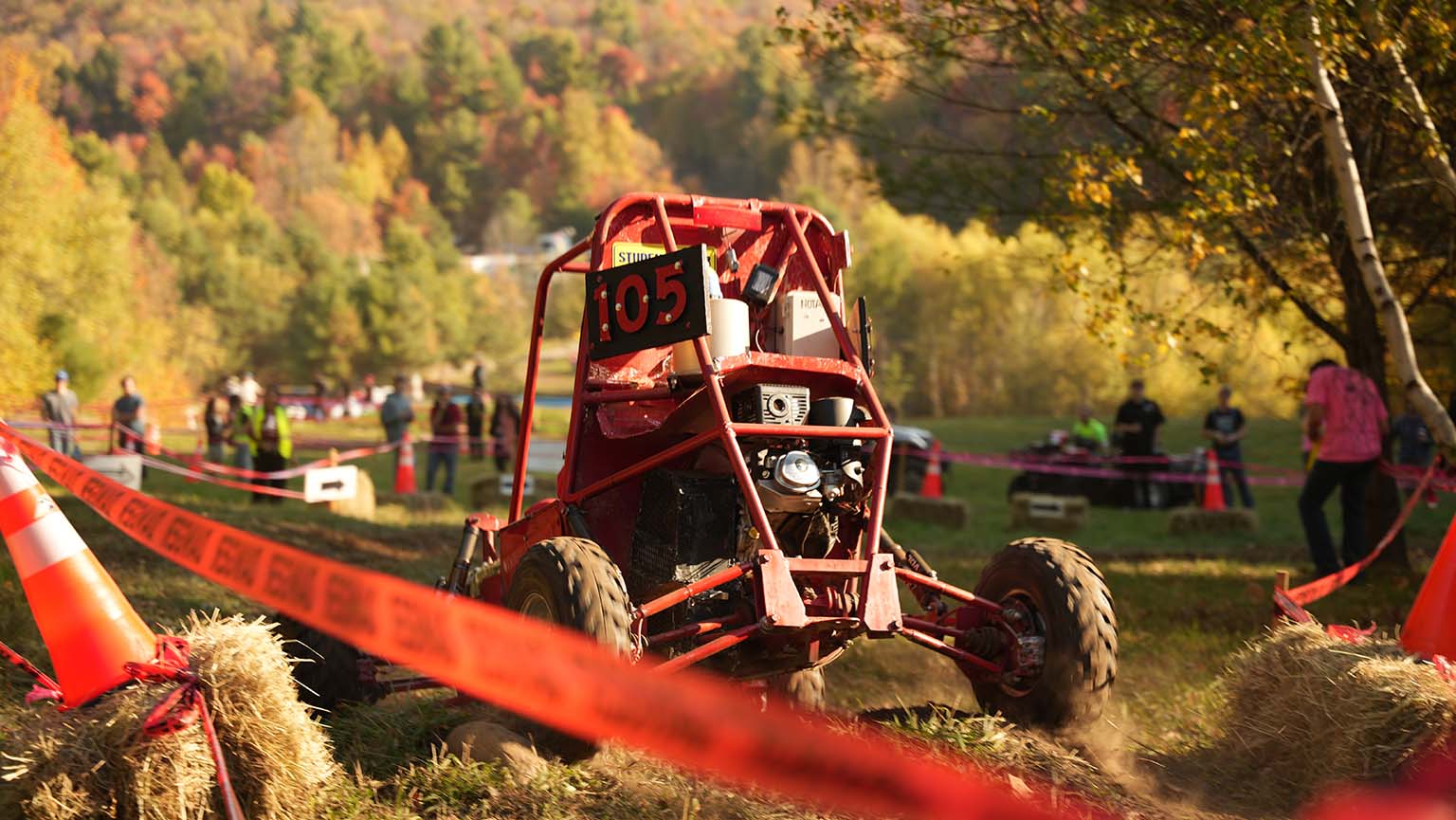 A bright red buggy speeds across a lush field, surrounded by nature.