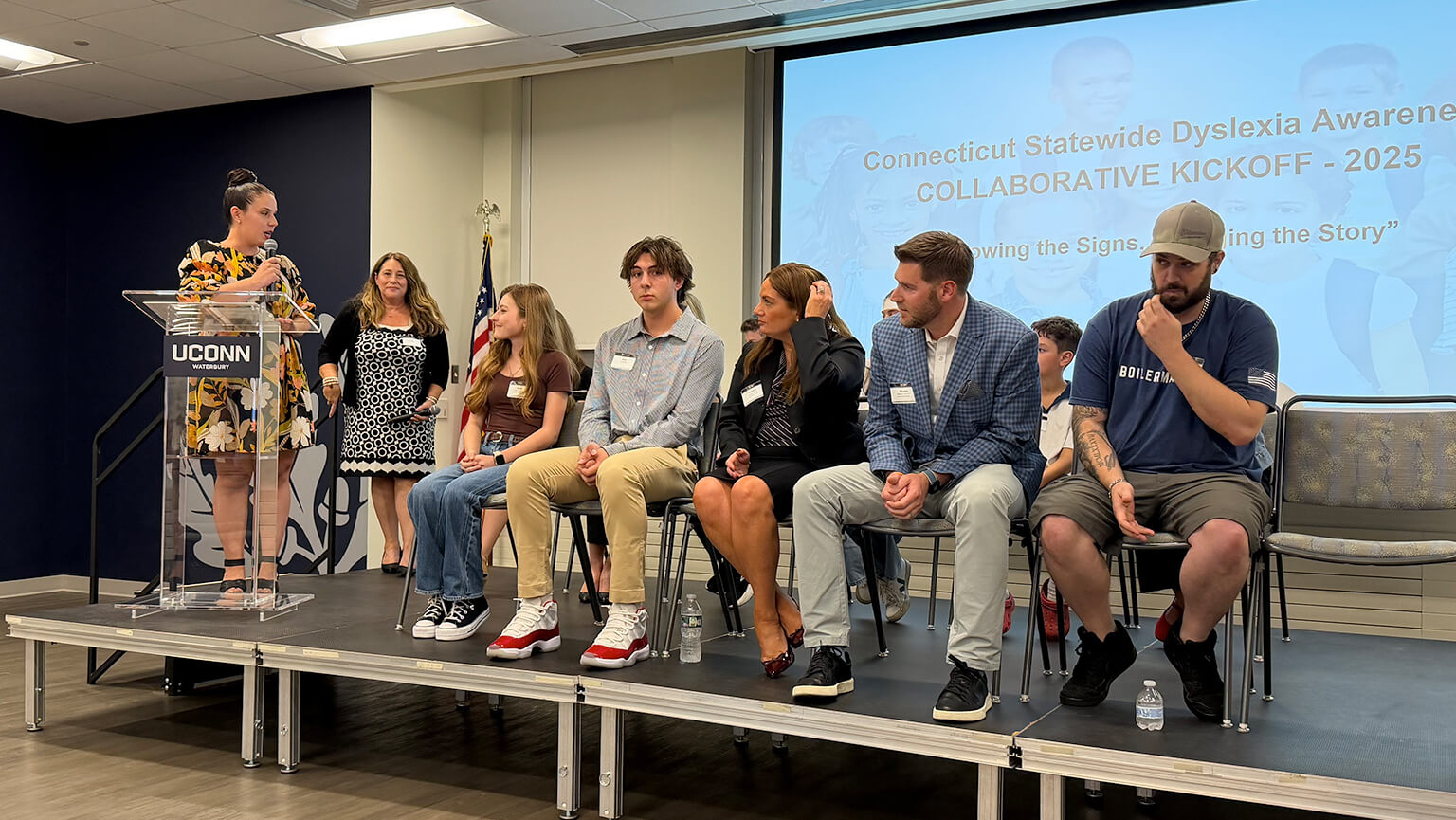 Several individuals on stage, engaged in a discussion while a speaker addresses the audience.