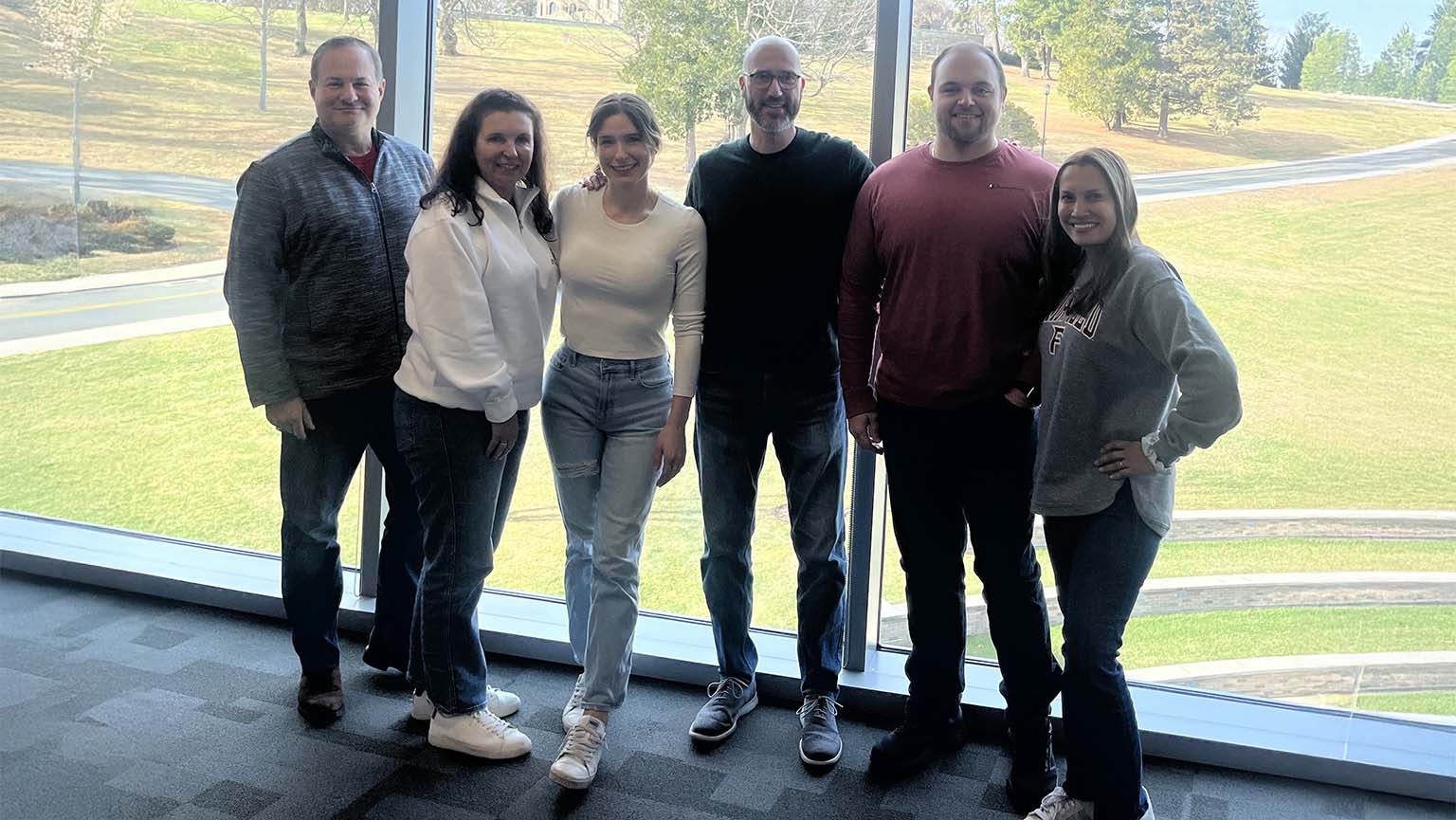 Several people gather in front of big windows, chatting and looking out at the scenery beyond.