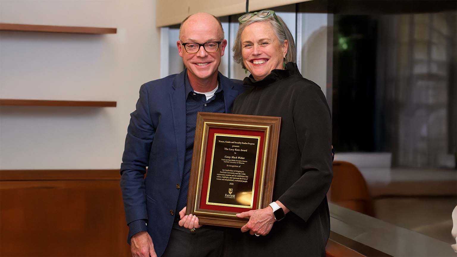 The person on the left is happily accepting an award from the person on the right in a festive setting.