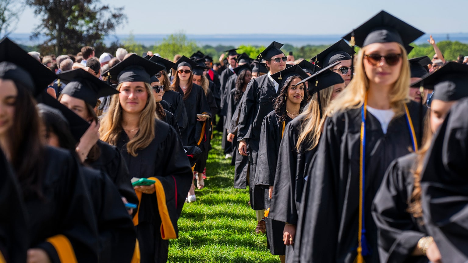 Undergraduate students in caps and gowns processing down Bellarmine Lawn for Fairfield's 75th Commencement ceremony.
