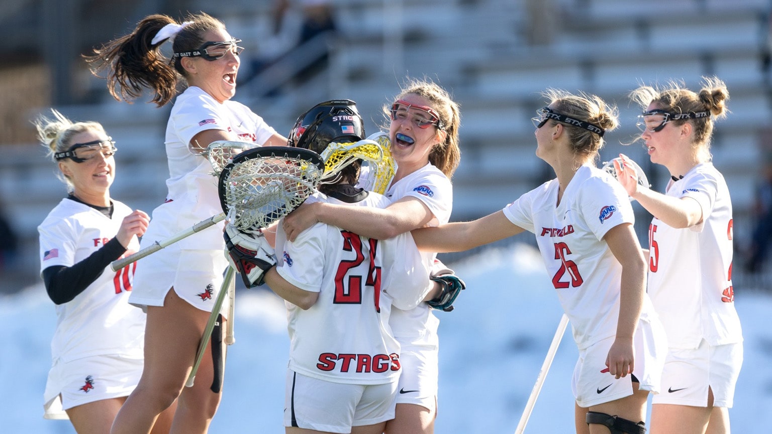 Women's lacrosse players celebrating a victorious game as the final score is announced.