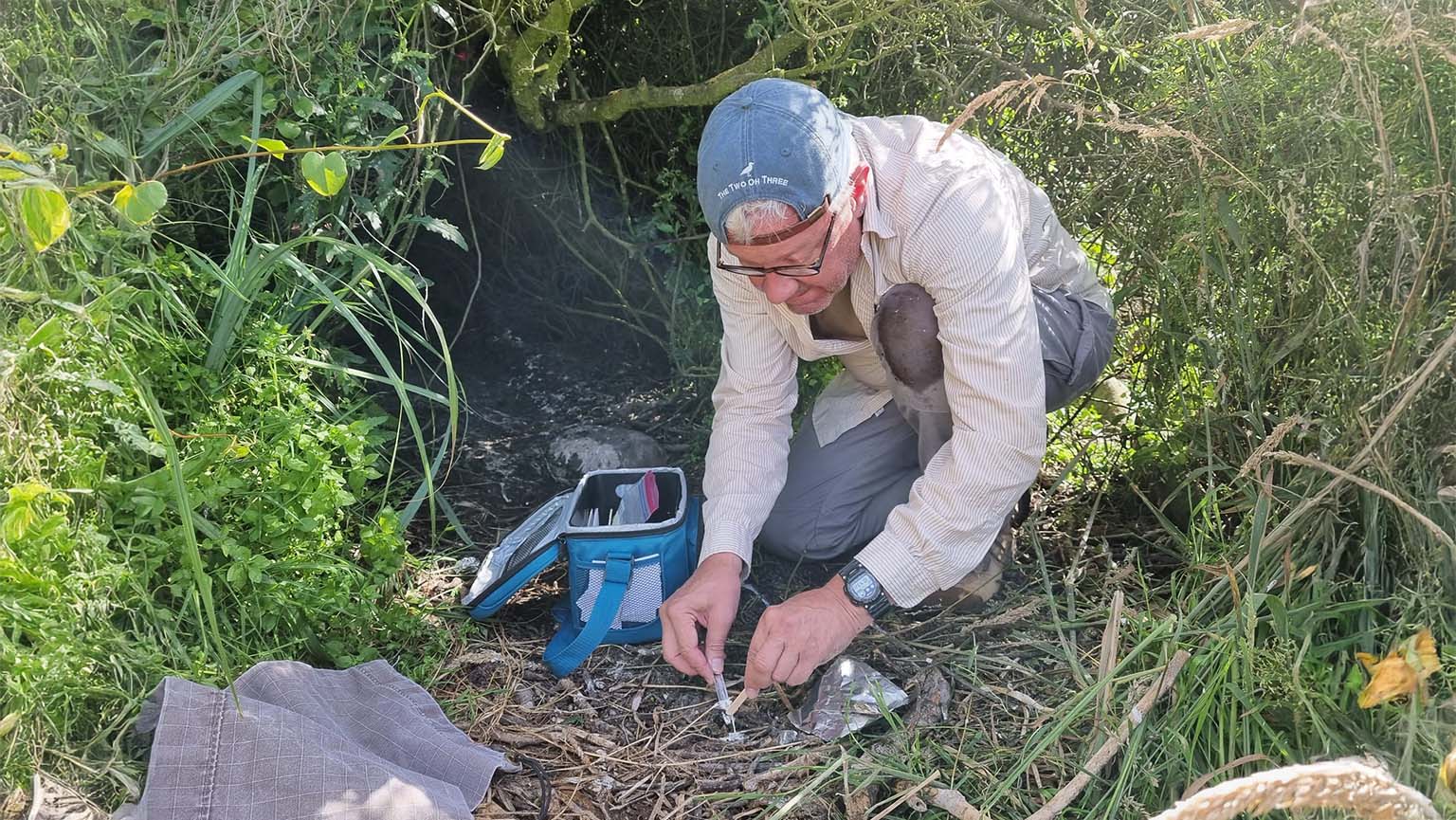 Image of a man kneeling in the grass, fixing a device while collecting samples for research.