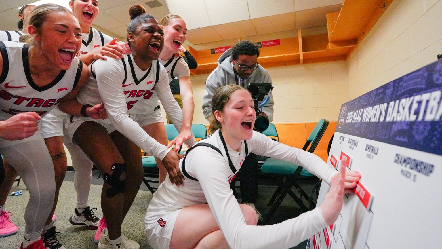 Fairfield Women's Basketball team placing their 'Fairfield' plaque in the winner's spot on th 2025 MAAC Championship matchup board.
