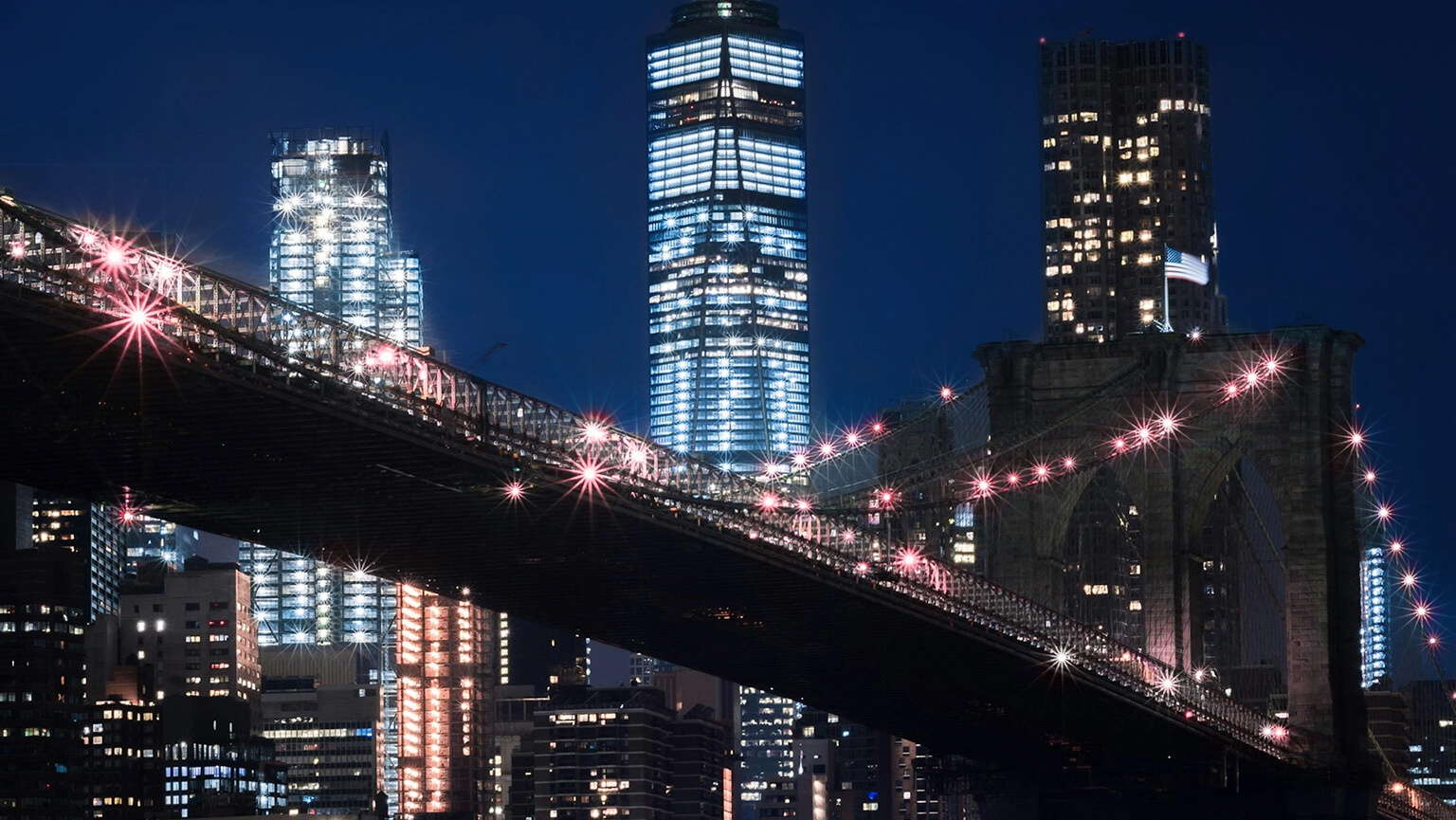 A nighttime view of the Brooklyn Bridge, illuminated against a dark sky, showcasing its iconic architecture and cables.