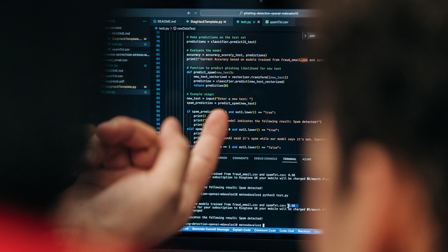 A student's hand points at a laptop screen displaying code in a dimly lit room. The focus is on the code, conveying concentration and technical detail.