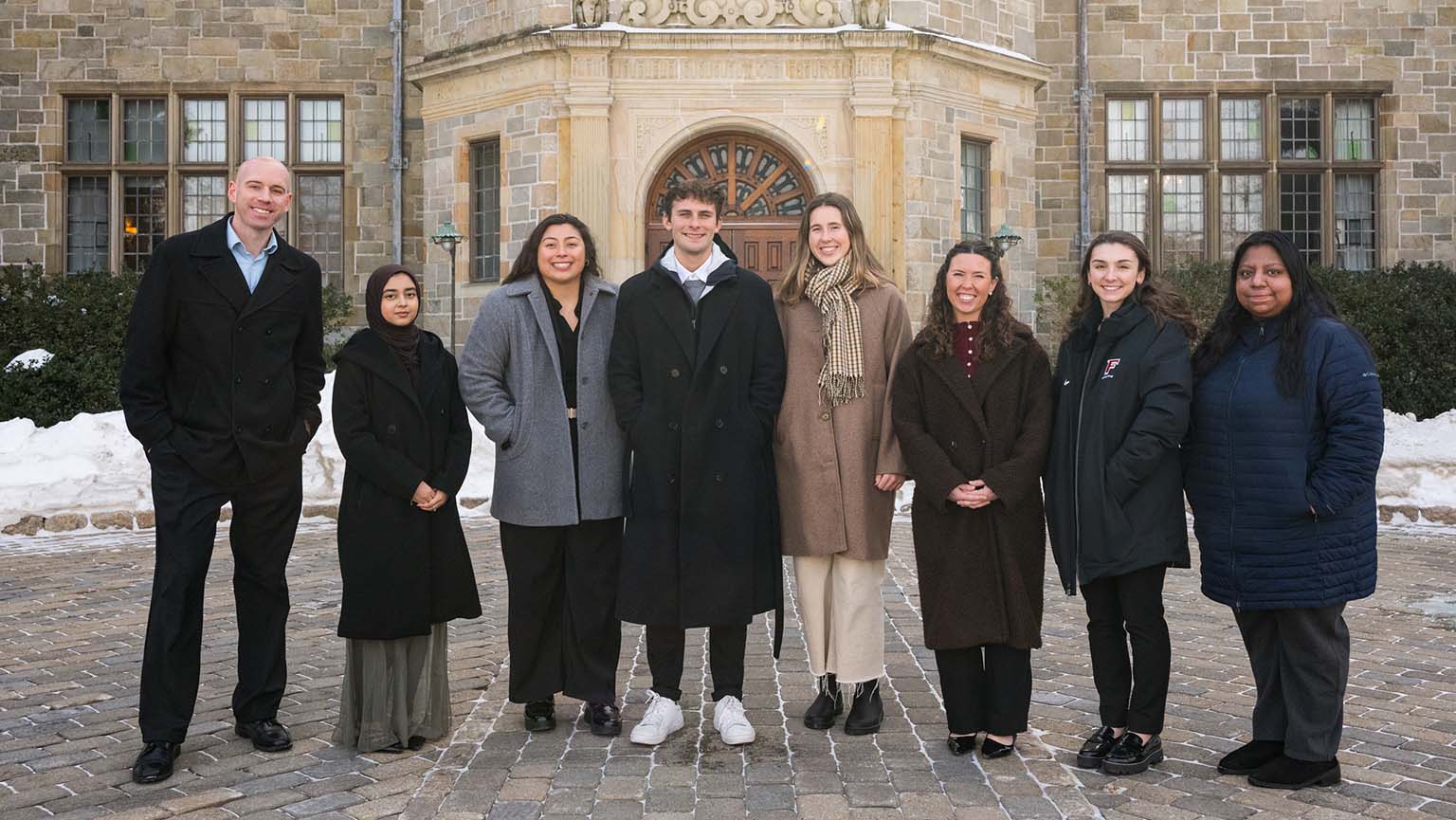 A diverse group of people posing in front of a building, looking happy and engaged.