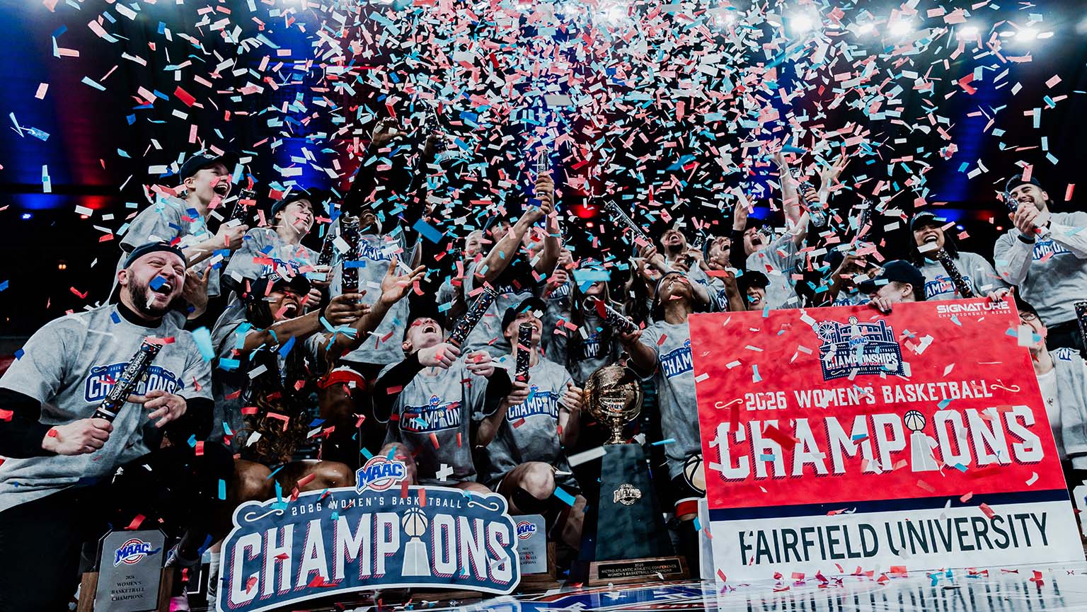 The women's basketball team joyfully celebrates their championship win, raising the trophy high in the air.