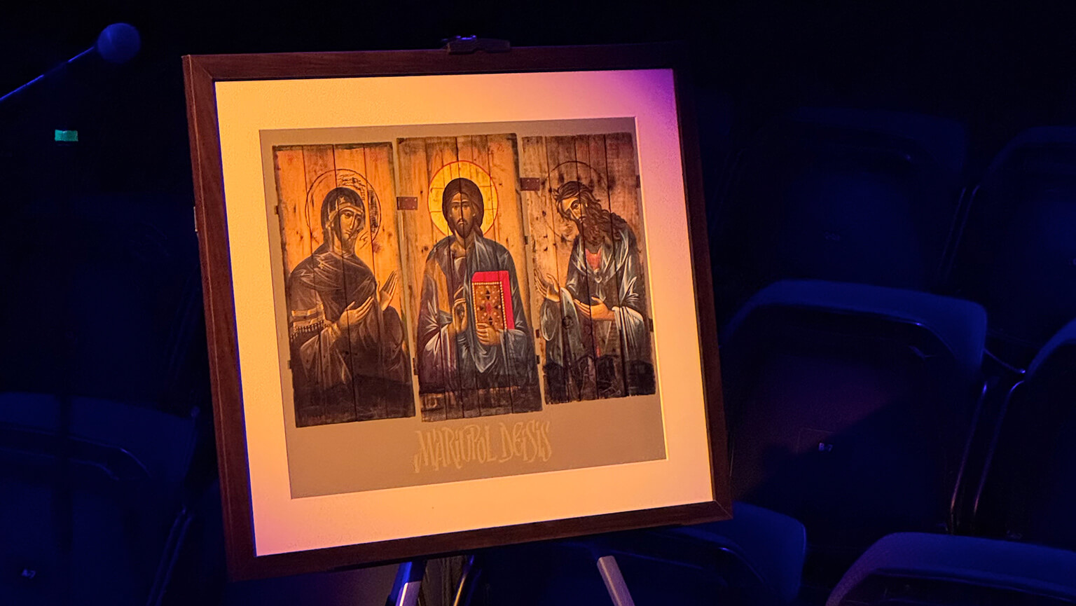 A framed photograph features three figures, each with halos, centered in soft light against a dark background. A serene, spiritual ambiance.