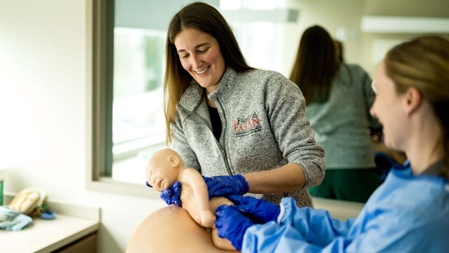 Nurse midwifery professor/director and student performing a midwifery simulation with manakins as part of provider training.