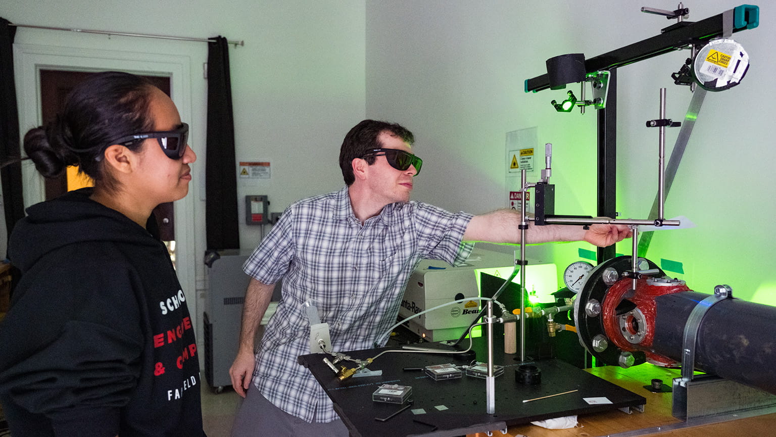 Engineering student and mentor wearing protective eyegear as they conduct experiments with a green, laser-based optical flow diagnostic system.