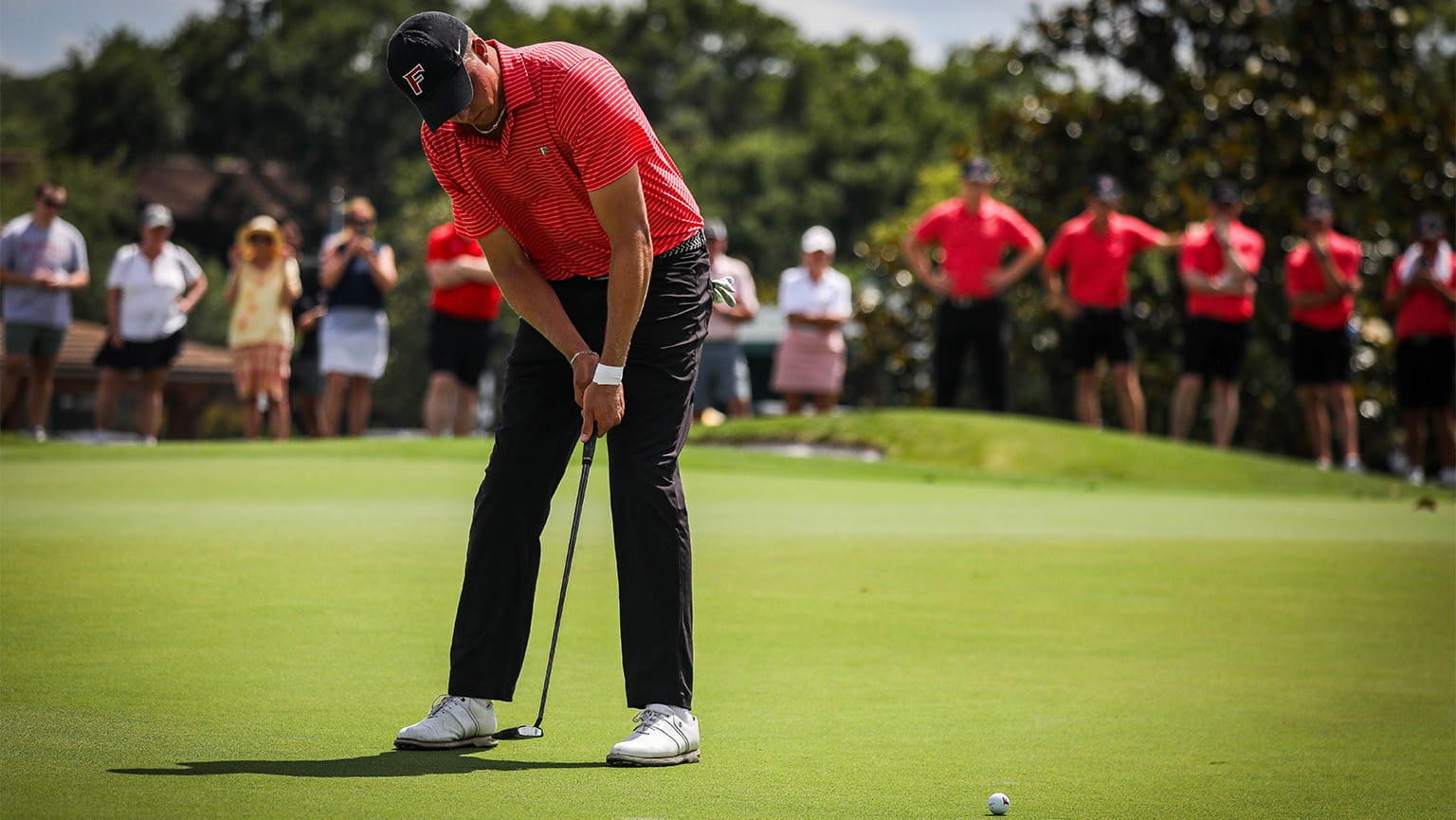 Sophomore golfer lining up a putt shot in front of supportive teammates and fans.
