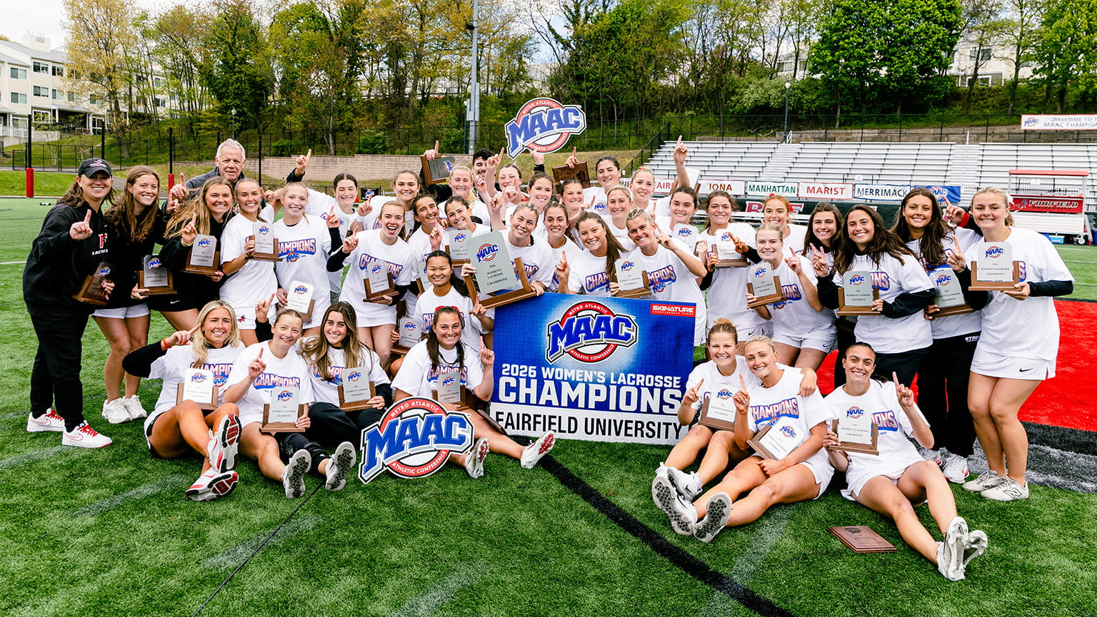 Women's Lacrosse team posing proudly in an all-inclusive group with their various 2026 MAAC Championship signage and awards.
