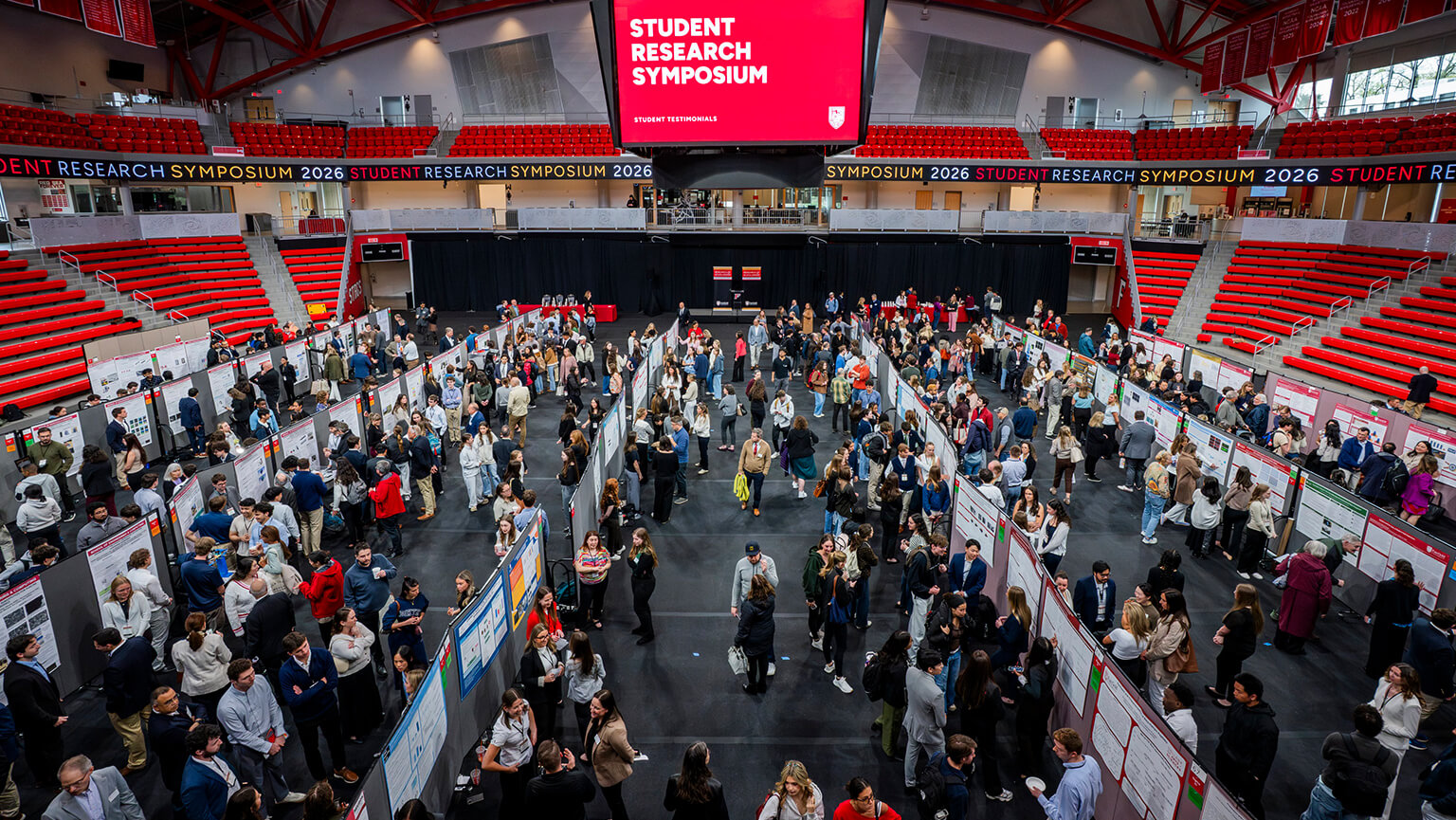 Wide view of a bustling Student Research Symposium at the Leo D. Mahoney Arena. Attendees study posters on display, creating an energetic and collaborative atmosphere.
