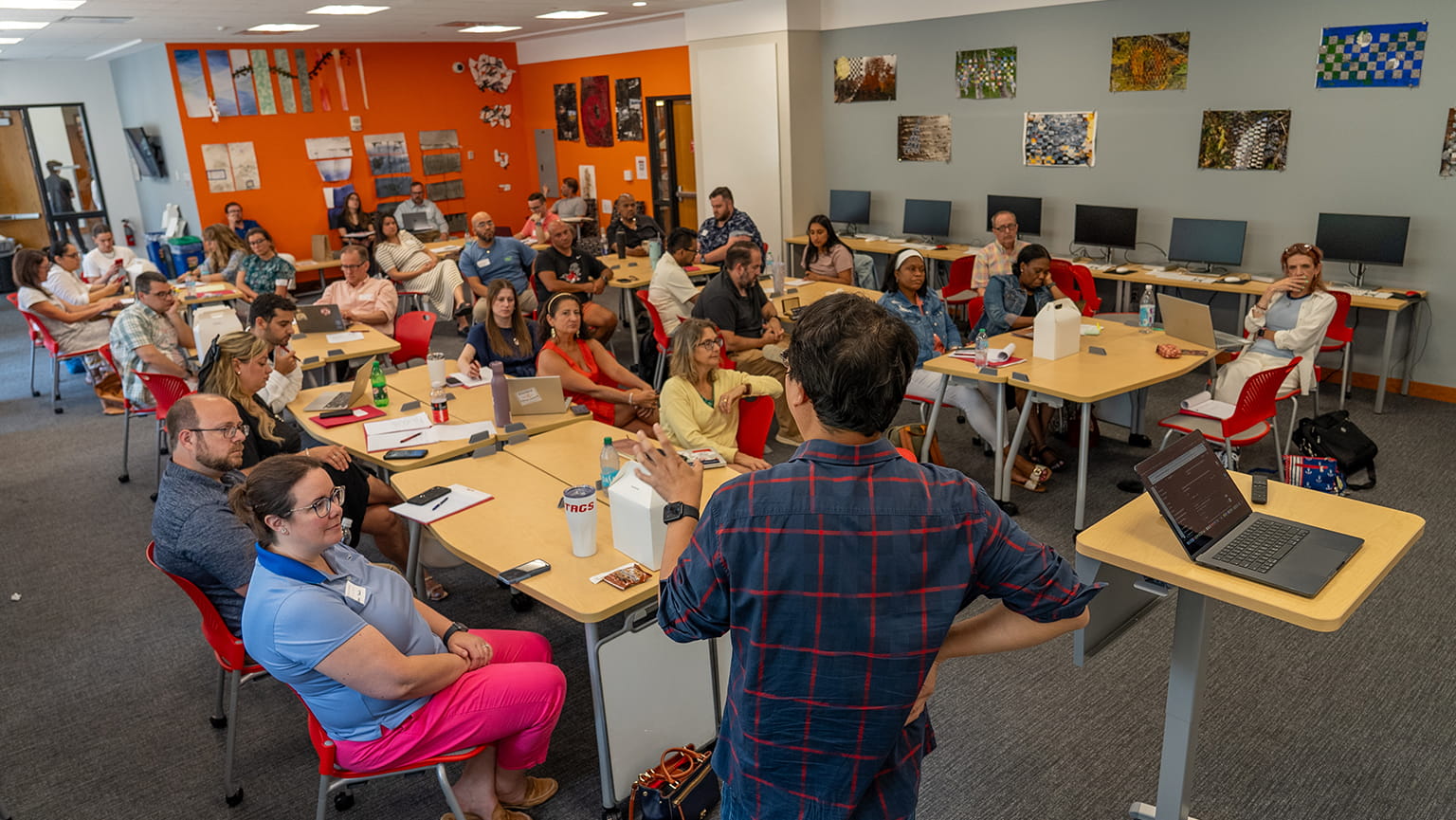 A classroom scene with a group of students seated at tables, engaged in discussion and learning activities. The scene is educational and professional.