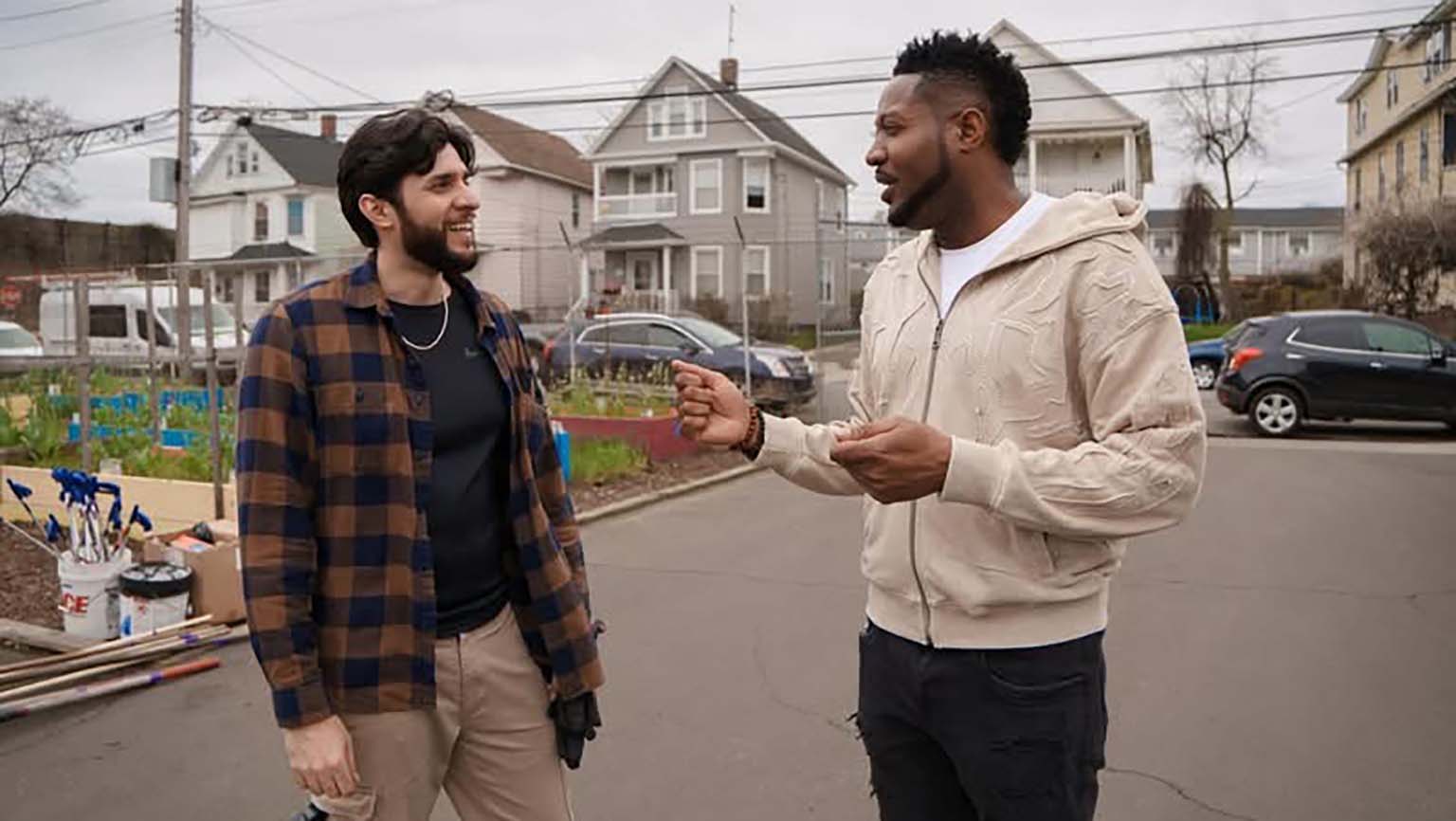 Two men engaged in conversation on a residential street, surrounded by houses.