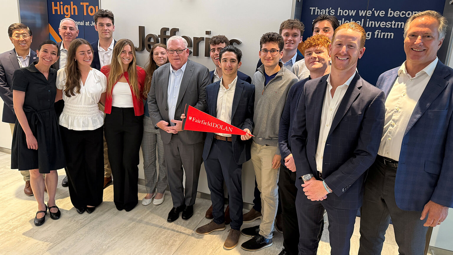 Fairfield Dolan faculty and students smiling at an event, gathered around a red ribbon, with a branded backdrop and an upbeat, celebratory mood.