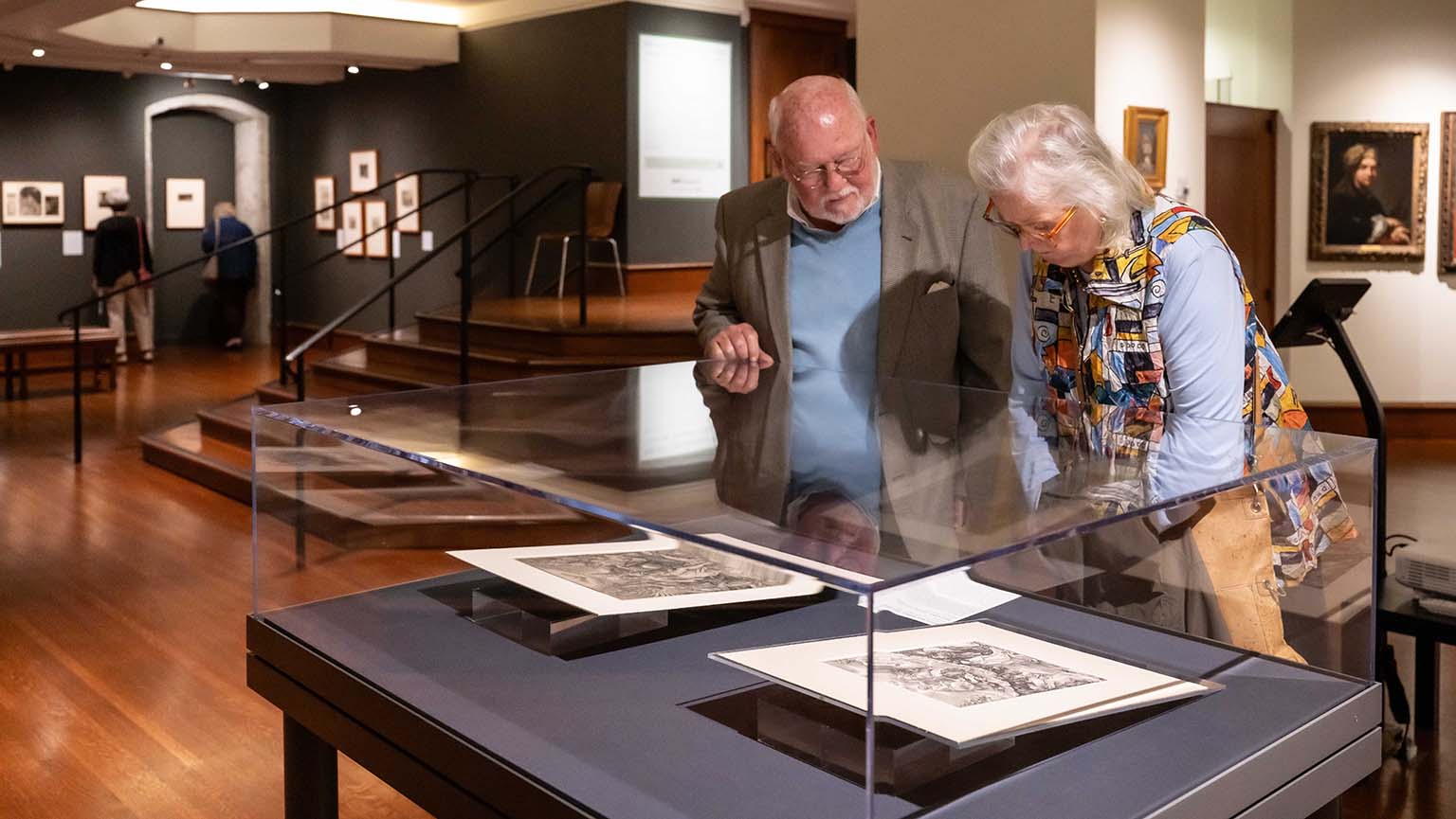 Two visitors admire a colorful painting in a museum, engaged in conversation about the artwork.