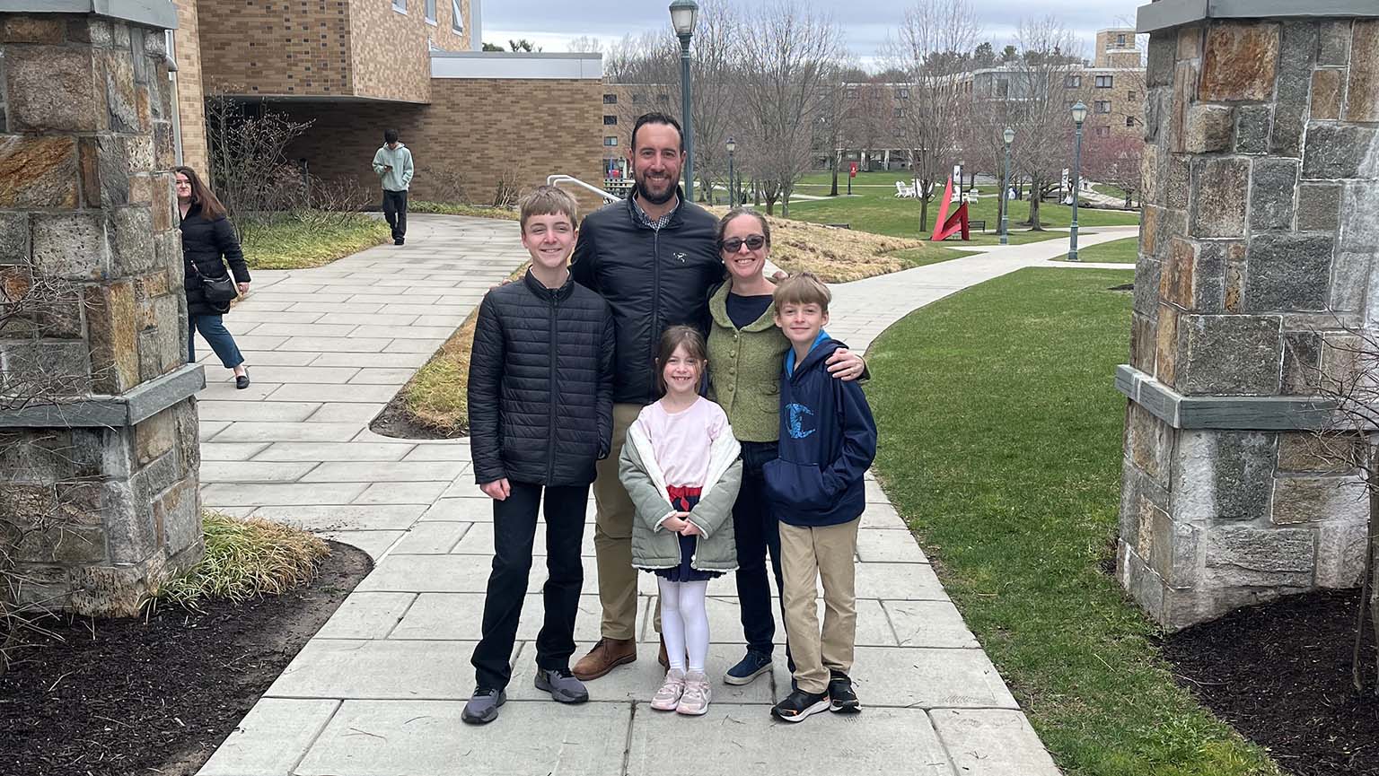 A happy family stands together in front of a charming stone building, smiling for the camera.