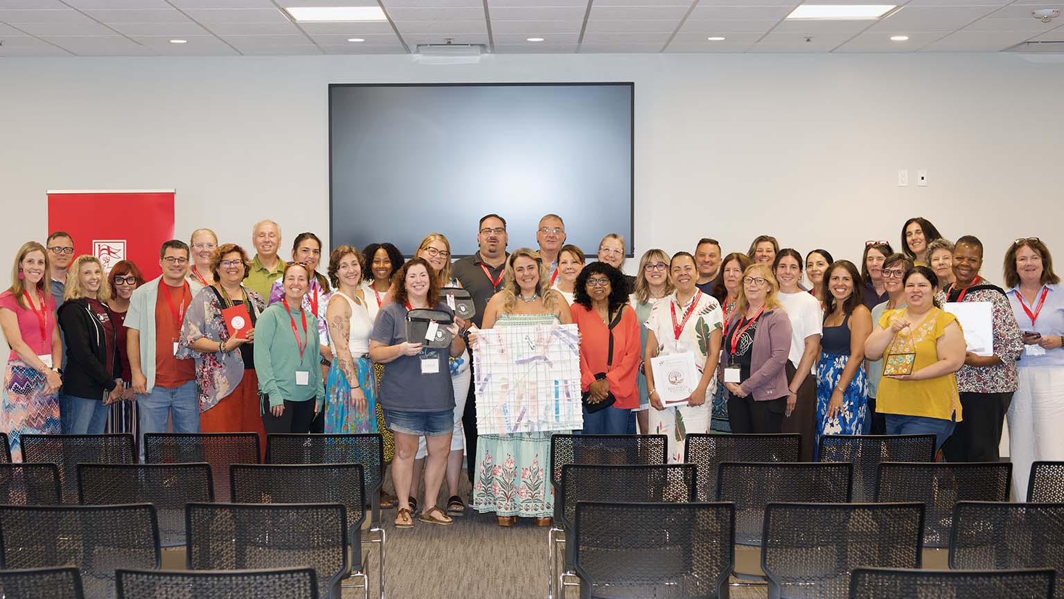 A diverse group of people in a room, engaged with a large screen that features a presentation or important content.