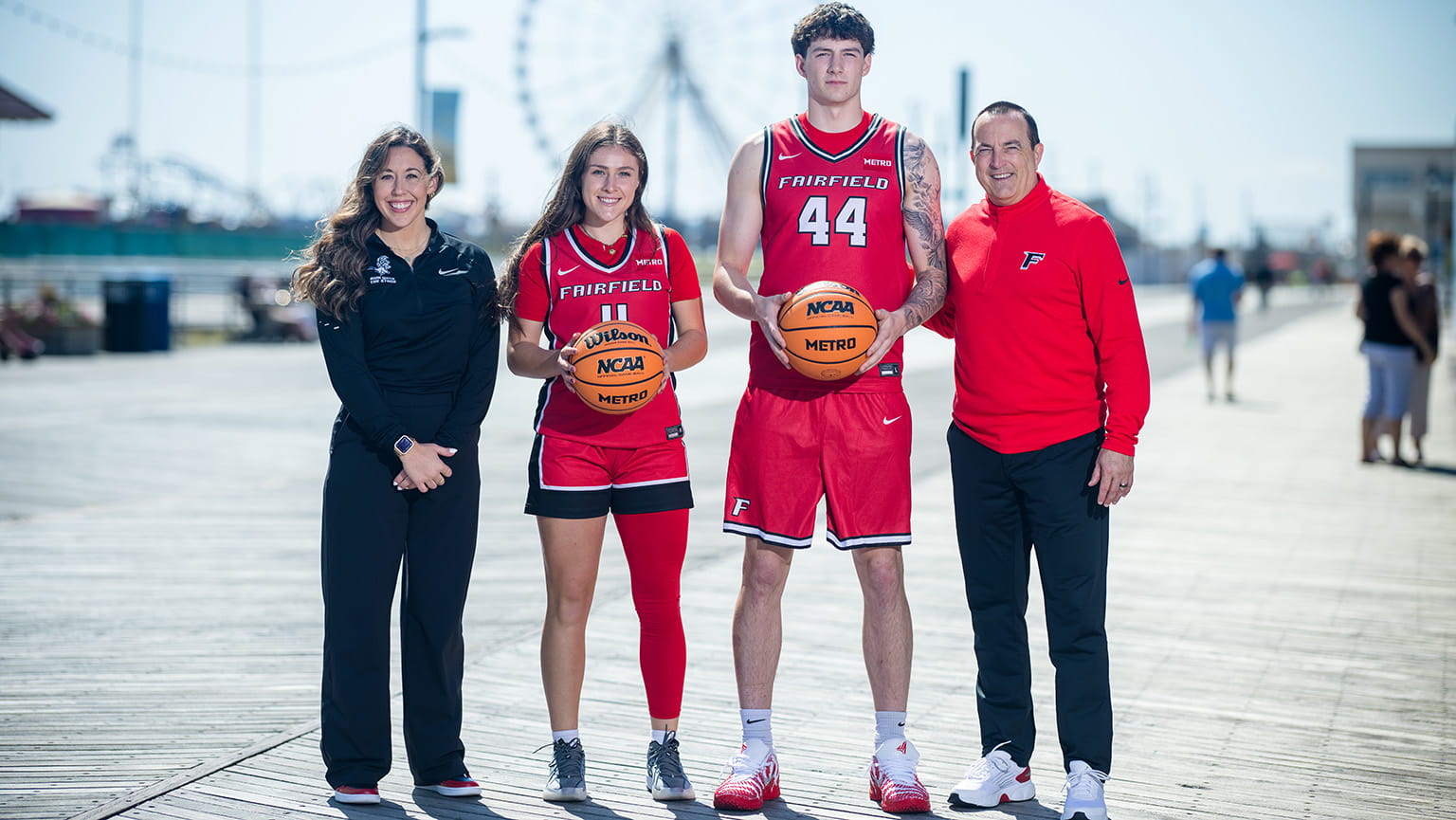 One graduate and one sophomore student-athlete for Fairfield's Women's and Men's Basketball teams (respectively) posing with basketballs and their coaches on a sunny boardwalk.