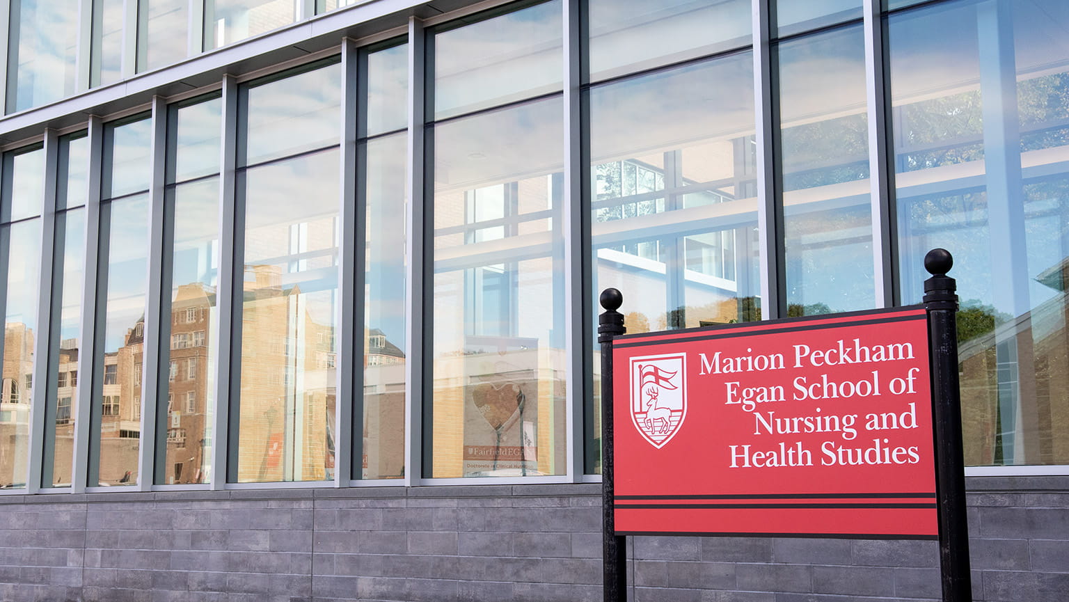 A close-up of the red, branded sign that reads 'Marion Peckham Egan School of Nursing and Health Studies', marking the modern, brick-and-glass building.