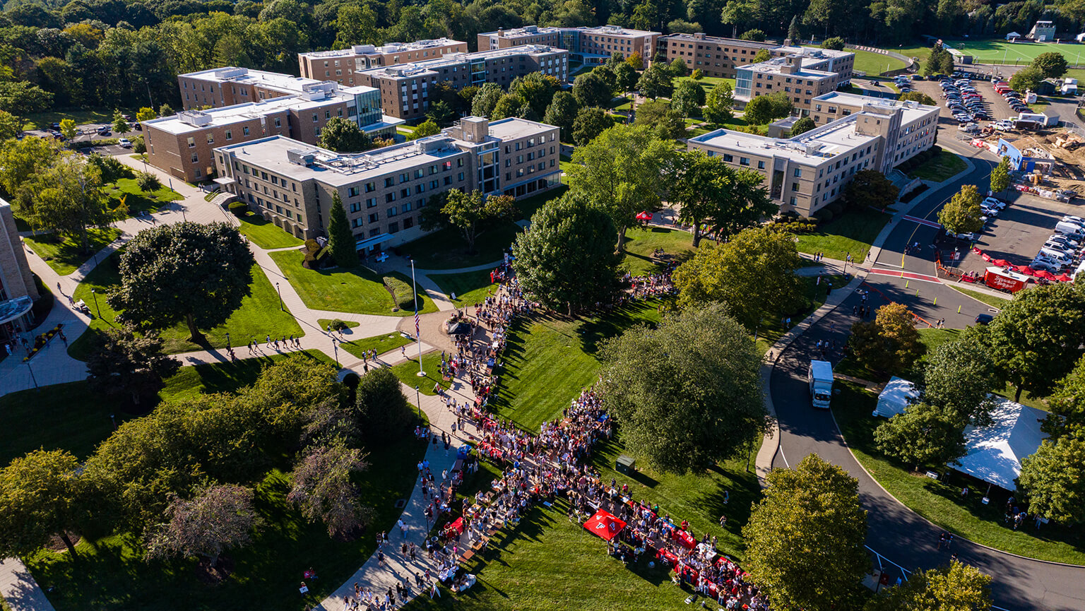 Aerial view of the Fairfield University campus as a large, colorful crowd gathers and marches along a central lawn, creating a lively community scene.