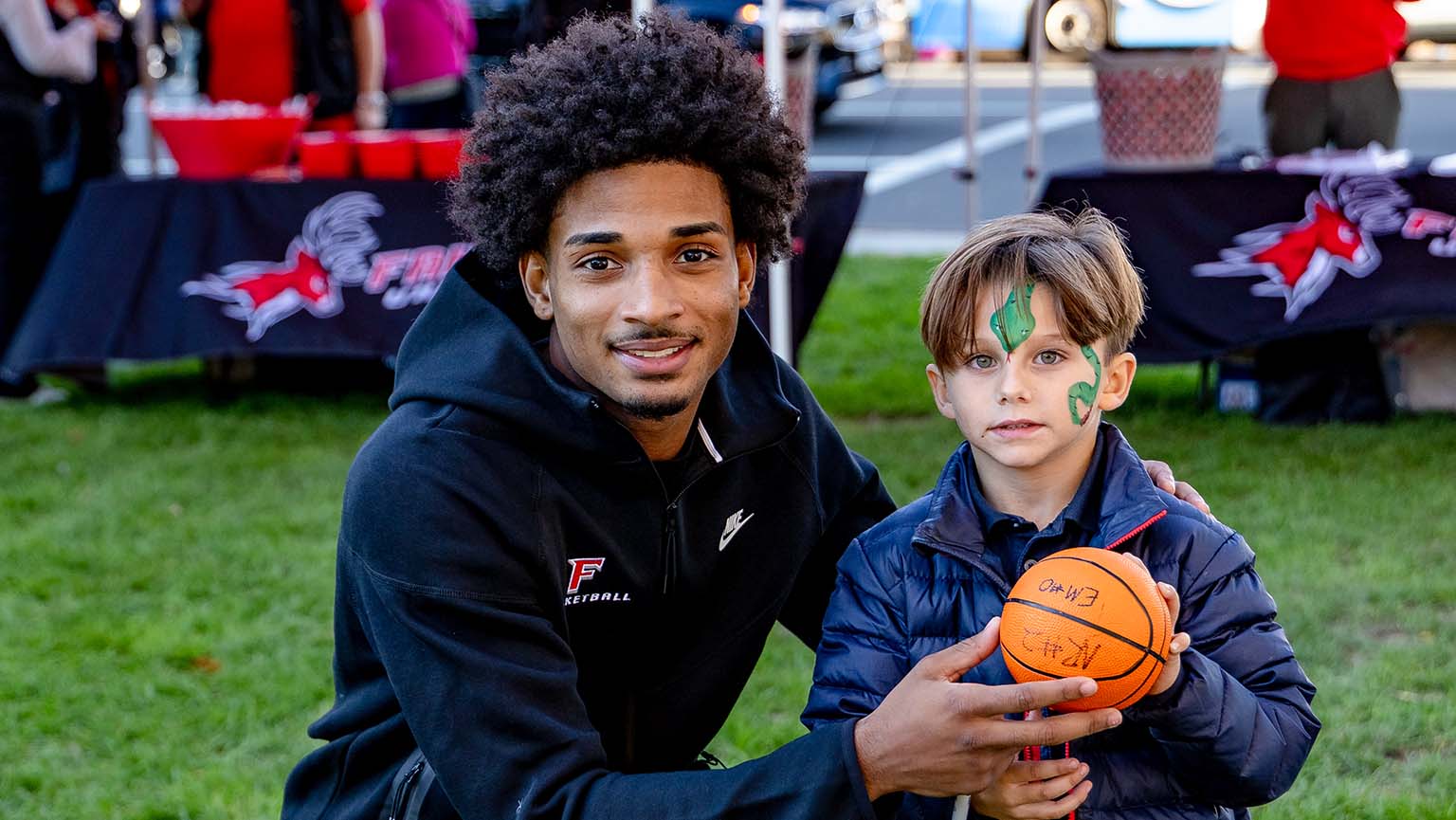 A man and a young boy stand together, each holding a basketball, smiling at the camera.