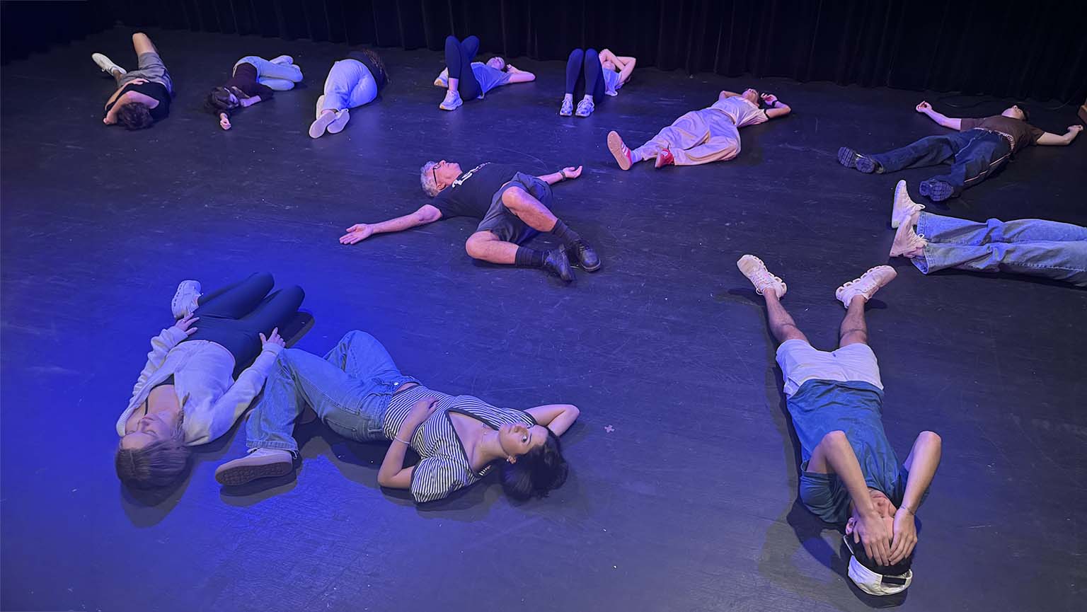 Several people resting on the floor in a dance studio, showcasing a moment of relaxation or teamwork during a session.