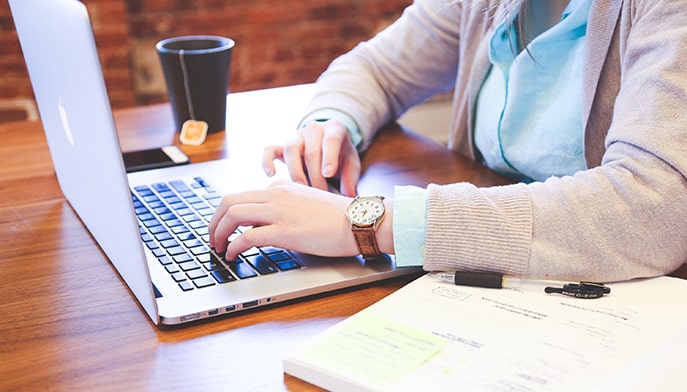 Professional employee typing an email on her laptop at her wooden, oak desk.