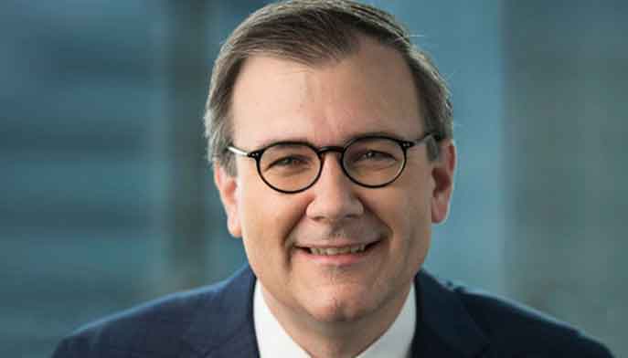 A man in glasses and a suit smiling confidently at the camera.