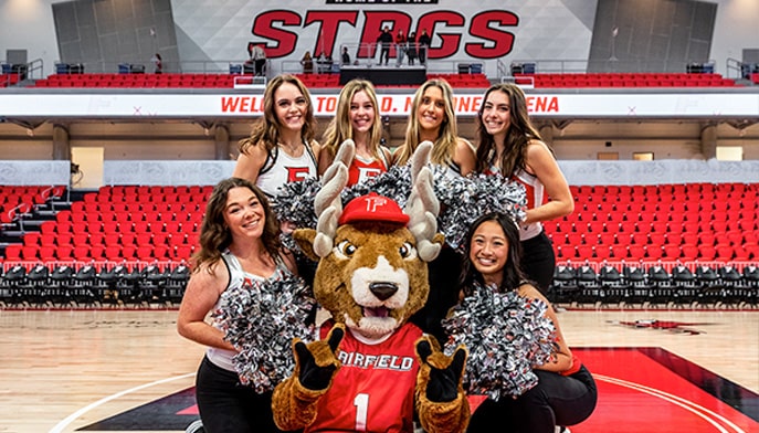 Six student cheerleaders posing for a picture with Lucas the Stag at half court at the Leo D. Mahoney Arena.
