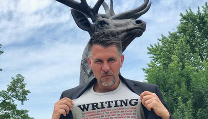Photo of Bryan Ripley Crandall grabbing the front of his shirt to show what it says.