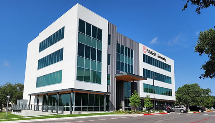 The crisp, clean, white exterior of the Fairfield University-branded Austin, TX School of Nursing campus on a clear, sunny day.