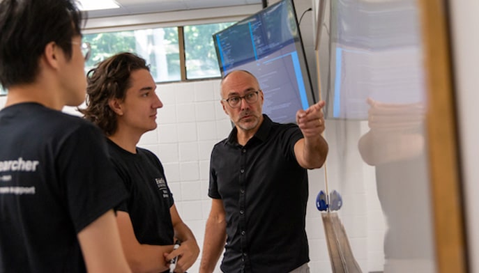 Faculty member pointing at white board with two students in classroom.