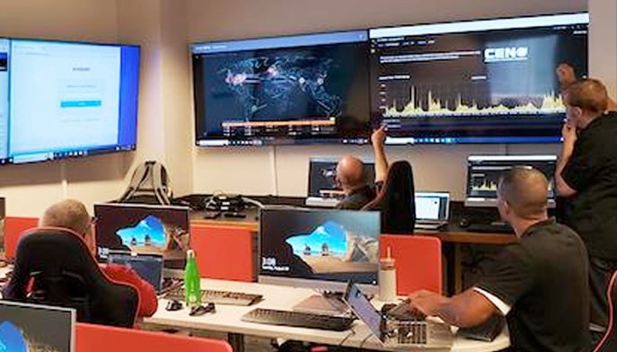Students in classroom setting pointing at large monitors on walls and talking to each other. 