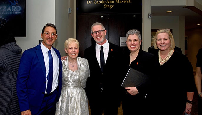 Dr. Maxwell posing with visiting alumni singers beneath new stage name sign.
