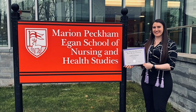 Gabby Kearney ’24 poses with her Sigma Theta Tau certificate and honor cords outside of the Egan School of Nursing and Health Studies.