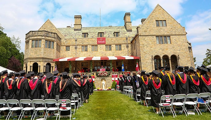 Graduates in gowns stand facing Bellarmine Hall at Commencement