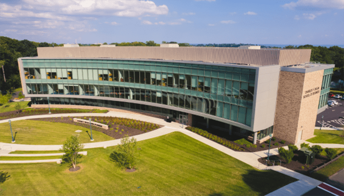 Exterior aerial shot of the brick-and-glass Dolan School of Business building overlooking a lush, green lawn.