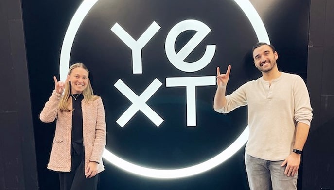 Students giving the Stags Up with their hands standing in front of a sign that shows a YEXT logo.