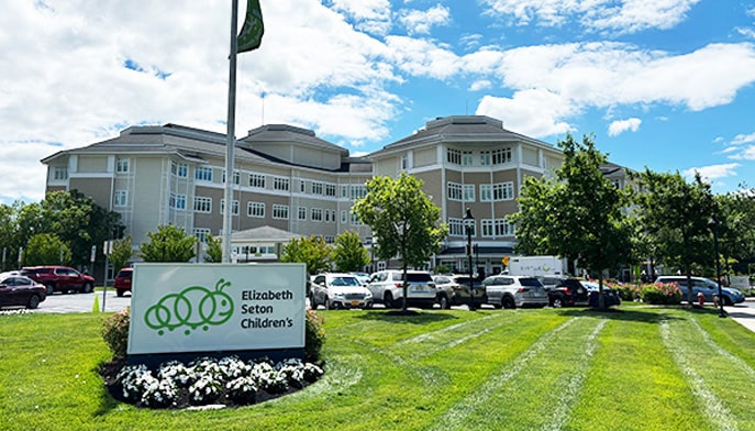 The front of the Elizabeth Seton Children’s Center on a bright sunny day, showing a sign and flag with building in background.