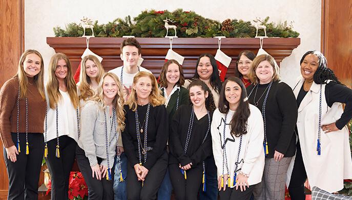 A cheerful gathering of students standing in front of a festive Christmas fire place, capturing a joyful moment in a photo.