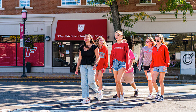 Several young women crossing a street in front of Fairfield University Bookstore, laughing and chatting as they navigate the urban environment together.