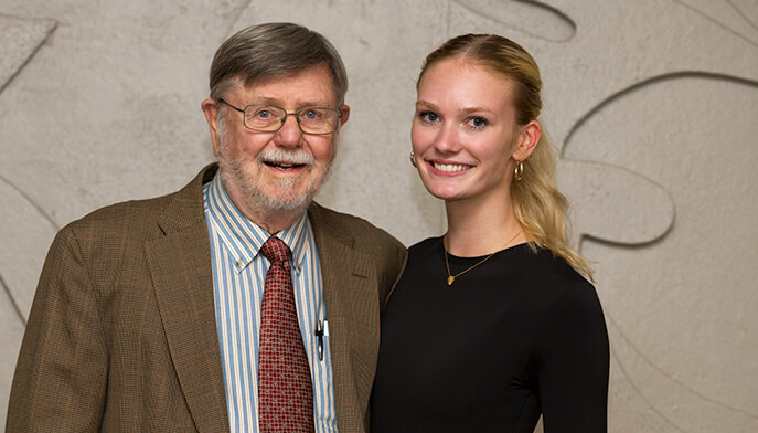 An older man and a young woman standing together, facing forward, with friendly expressions.