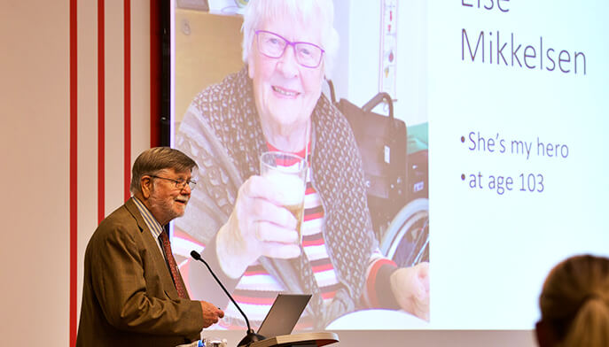 A man presenting information to an audience, using a projector and slides in a professional setting.