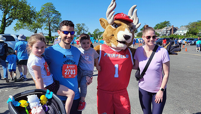 A cheerful family stands with a Lucas the stag mascot at a race, capturing a joyful moment of celebration and community spirit.  