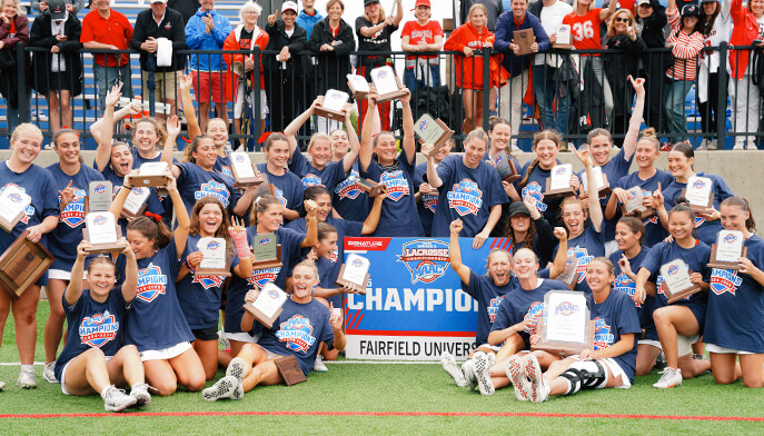 Fairfield University women's lacrosse team proudly poses together with their championship banner, celebrating their victory.  